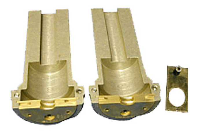 Twee messing behuizingen naast een rechthoekig metalen stuk met rond gat.