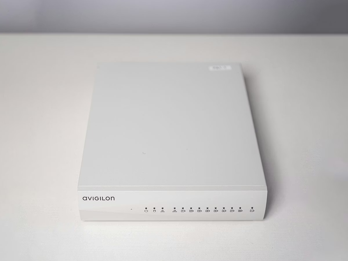 Wit elektronisch apparaat op lichte tafel met Avigilon-logo en LEDs.