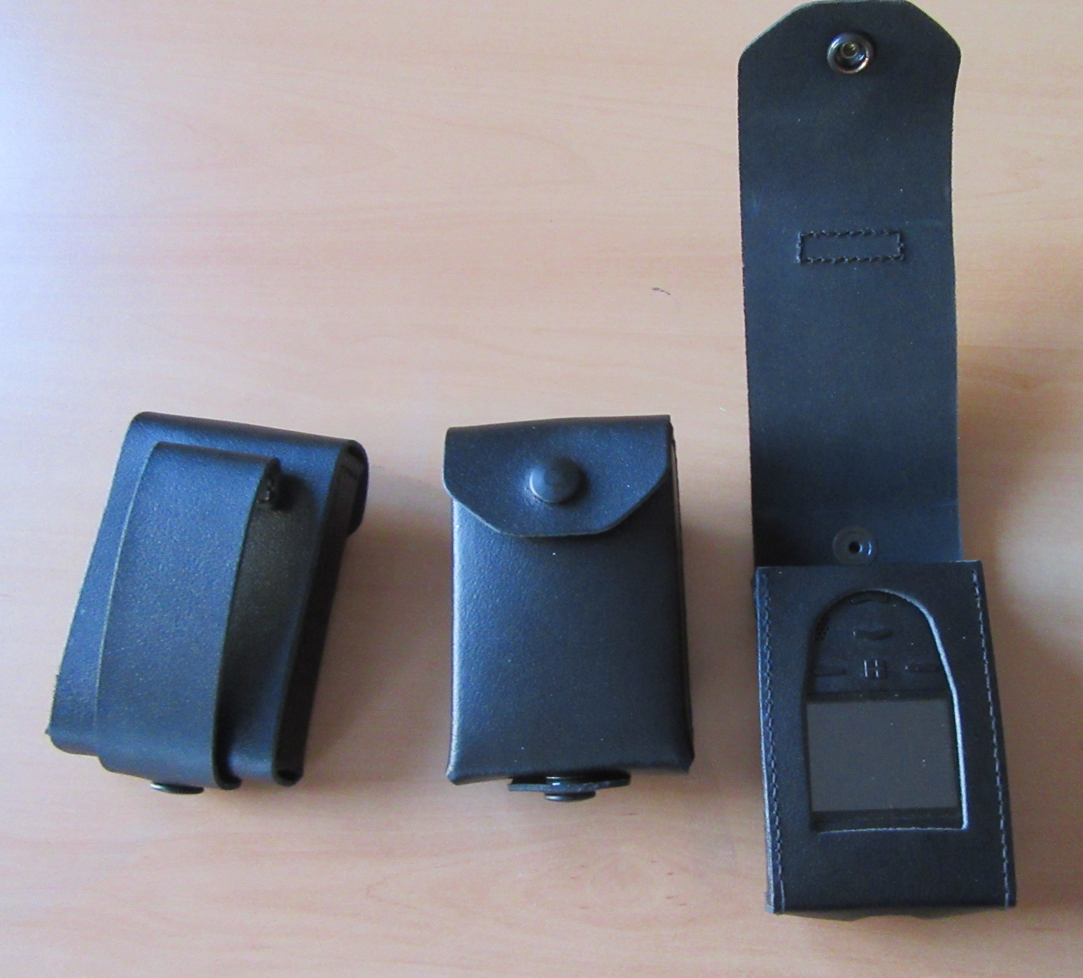 Trois étuis en cuir noir sur une table, deux fermés, un ouvert avec une fenêtre.