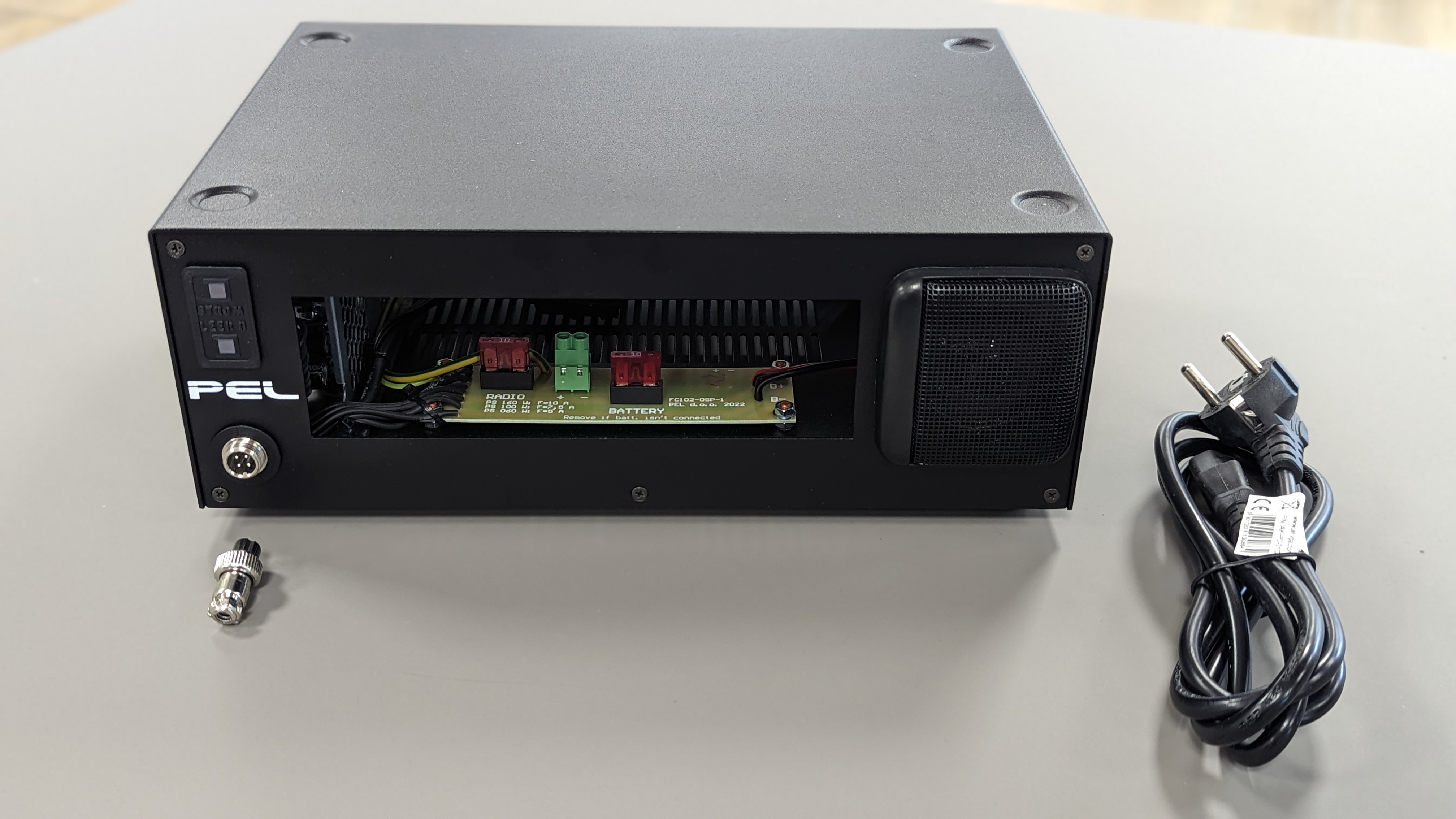 Zwarte doos, open voorkant met bedrading, connector en stroomkabel ernaast.