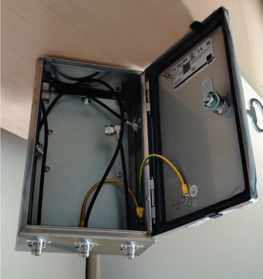 Metalen behuizing met open deksel, binnen gele en zwarte kabels zichtbaar.