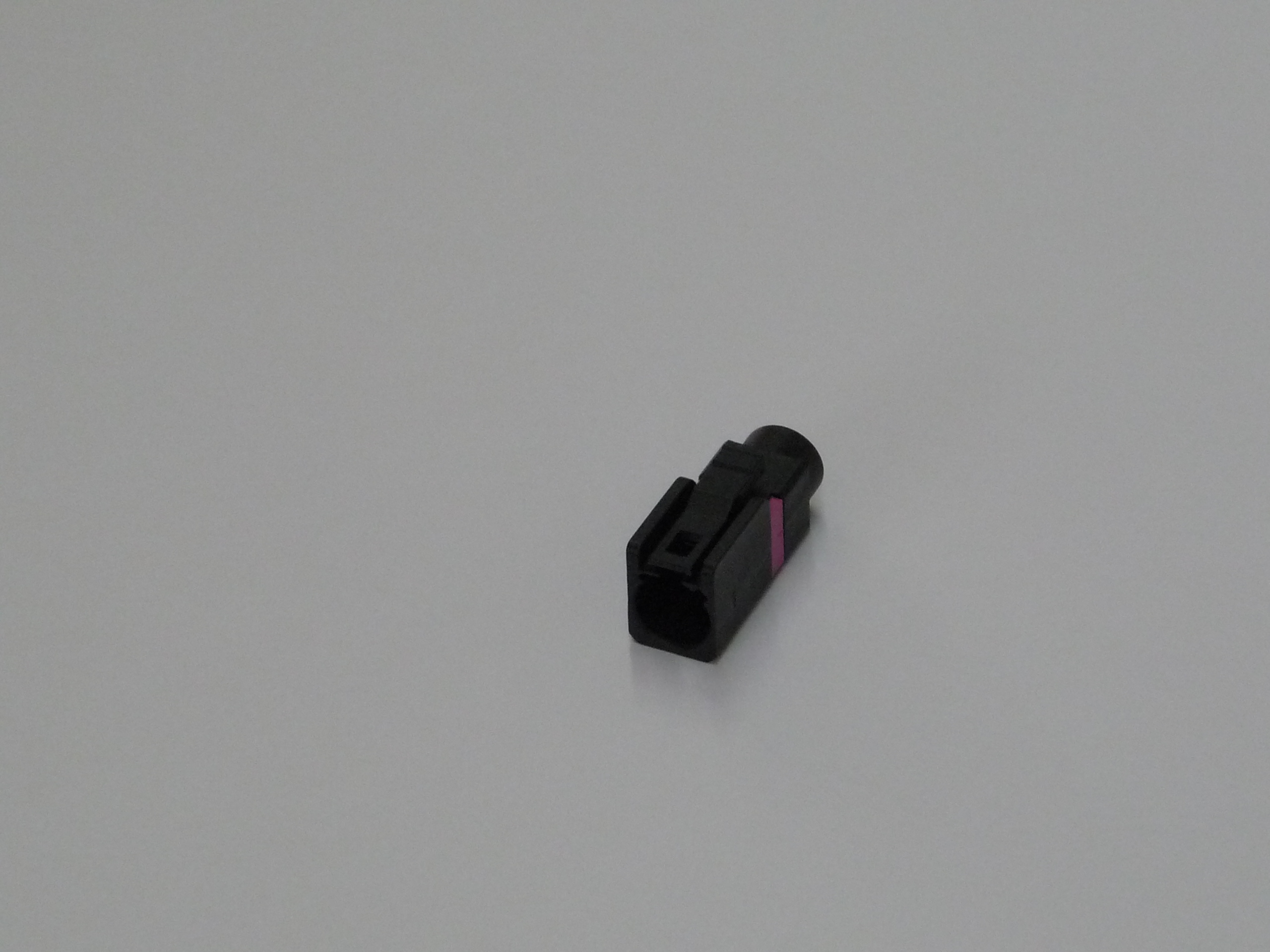 Zwarte elektrische stekker met roze element op grijze achtergrond.