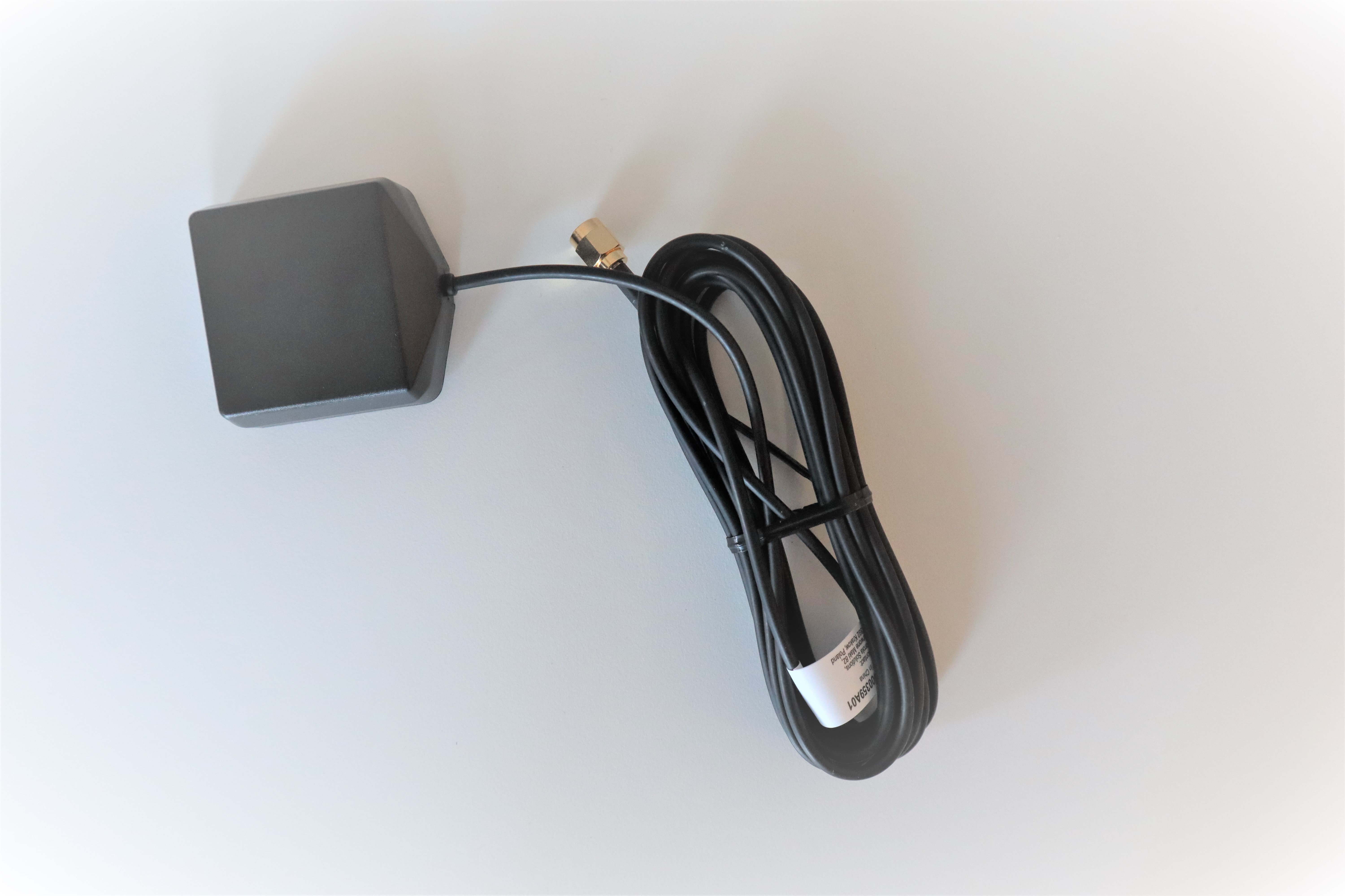 Zwarte vierkante GPS-antenne met lange kabel op witte achtergrond.