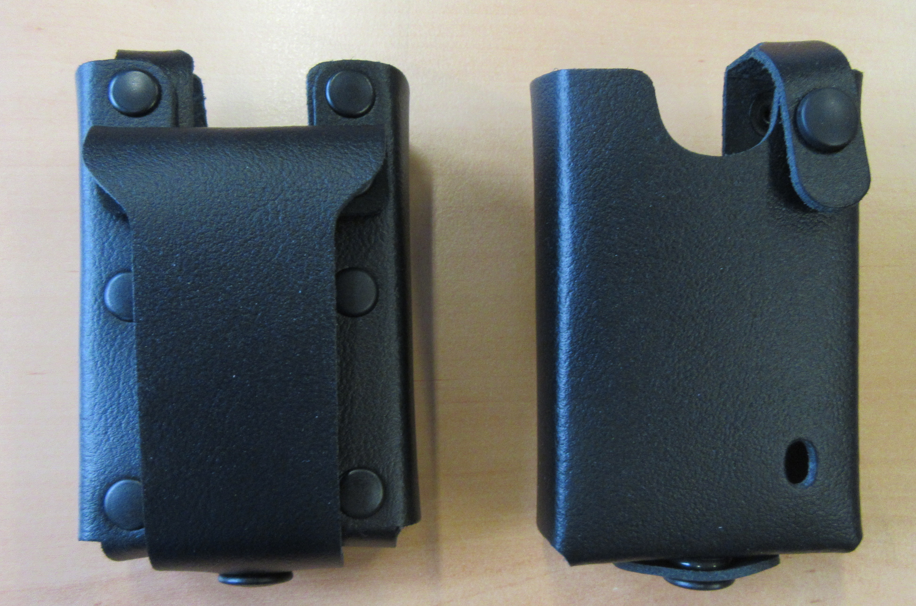 Twee zwarte leren hoesjes met drukknoopsluitingen op houten oppervlak.