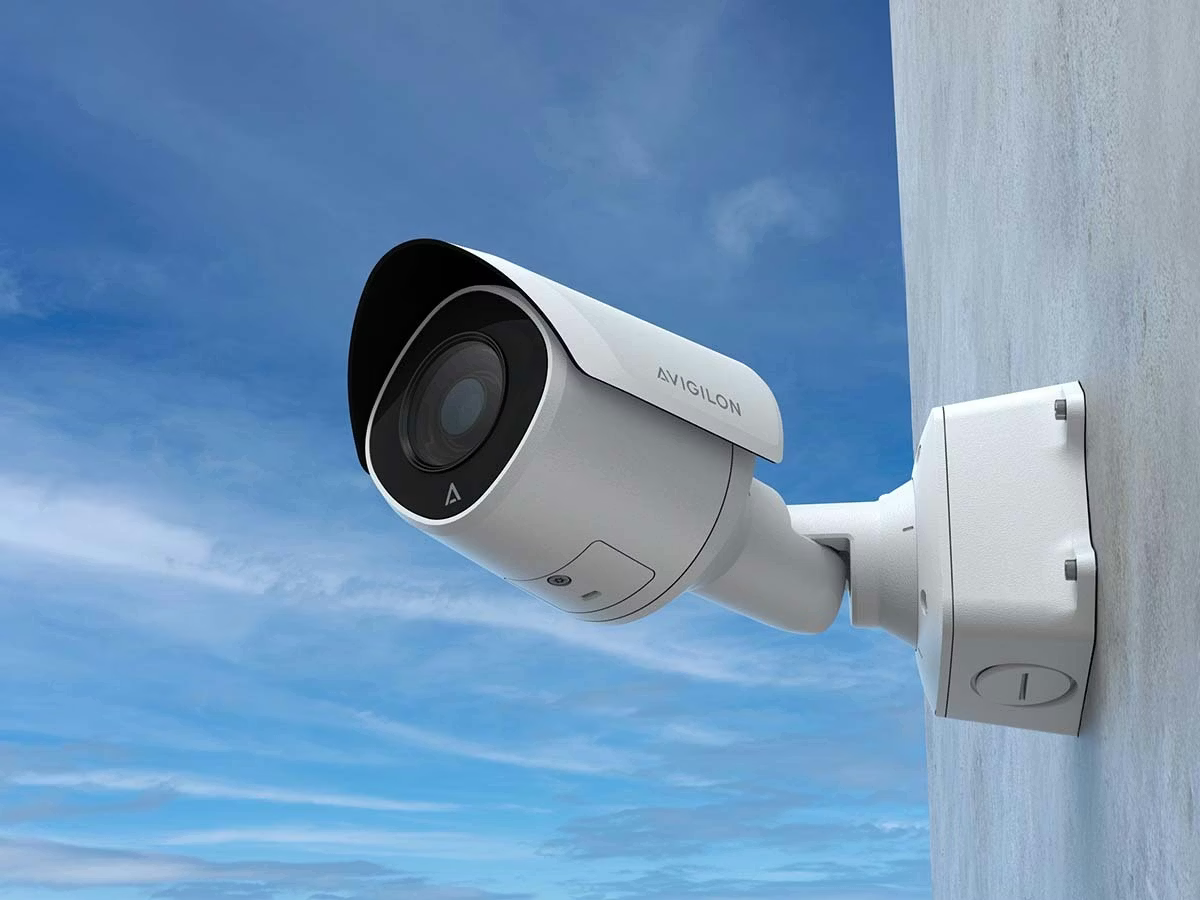 Wall-mounted surveillance camera against blue sky.