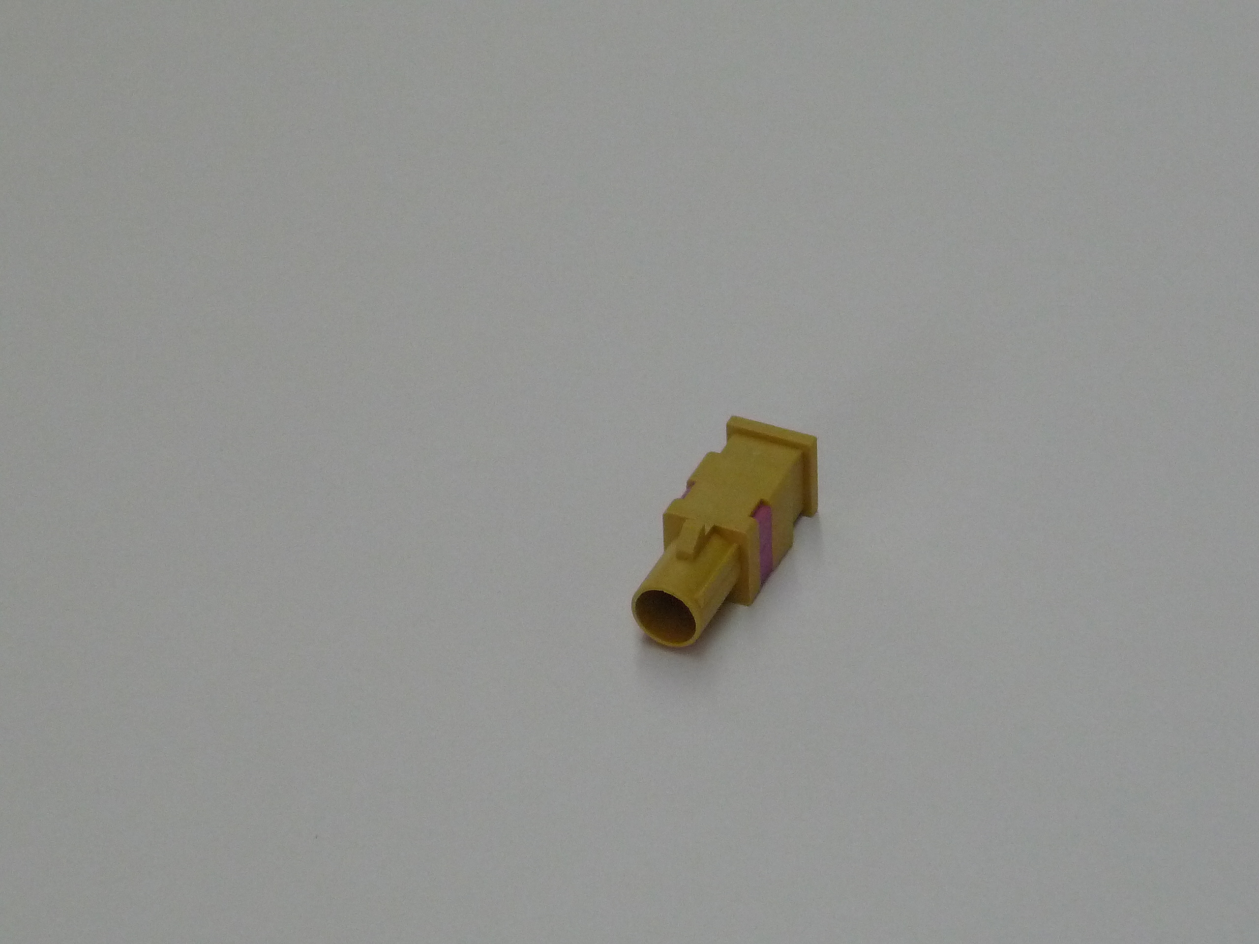 Kleine gele kunststof connector op grijze achtergrond.